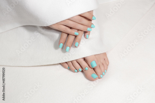 Beautiful pedicure and manicure. Close-up of pretty female toes and fingers with mint color nails. Feet and hands are covered with whte blanket.  photo