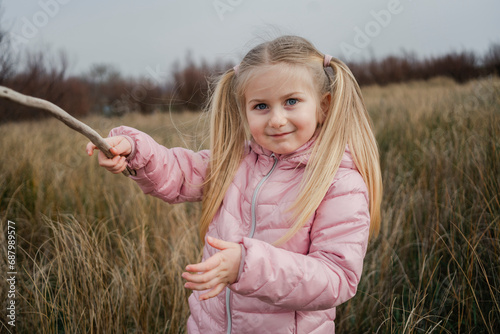 A young girl brandishes a stick like a sword, playing hero in the wild grass of an open field