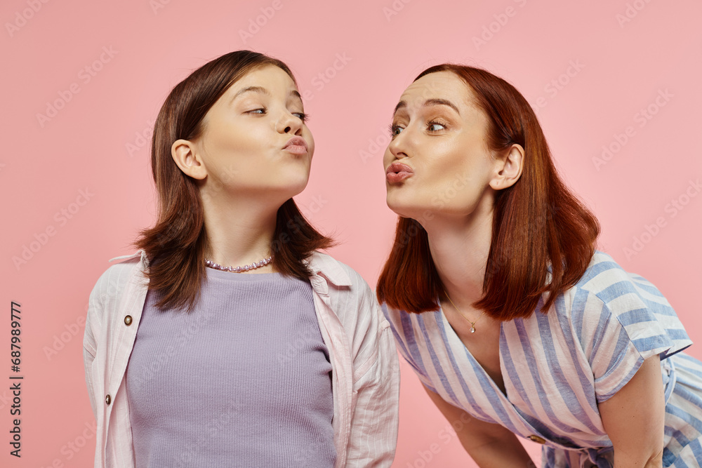 cheerful mother and teenage daughter pouting lips and looking at each other on pink backdrop cheerful mother and teenage daughter pouting lips and looking at each other on pink backdrop