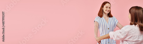 joyful and trendy woman with teenage daughter holding hands on pink backdrop, horizontal banner