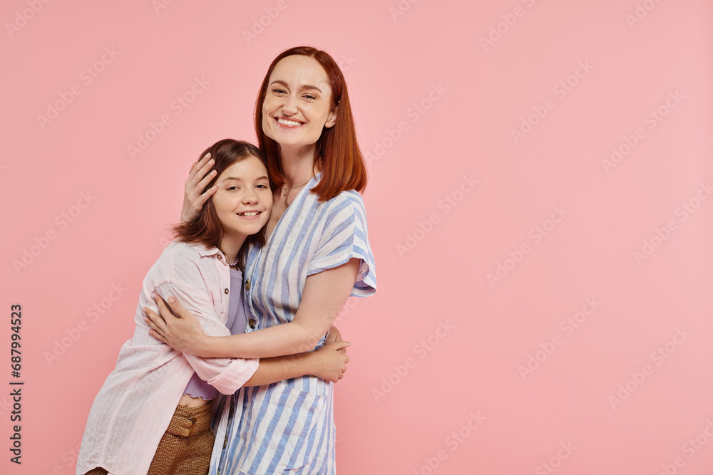 happy woman with teenage daughter in stylish casual attire looking at camera on pink backdrop happy woman with teenage daughter in stylish casual attire looking at camera on pink backdrop
