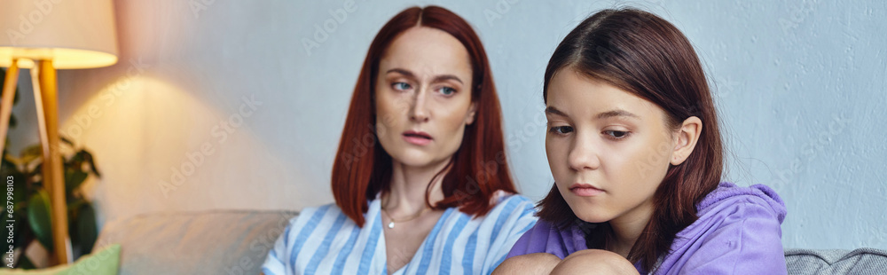 worried and caring mother looking at depressed teenage daughter on couch in living room, banner worried and caring mother looking at depressed teenage daughter on couch in living room, banner