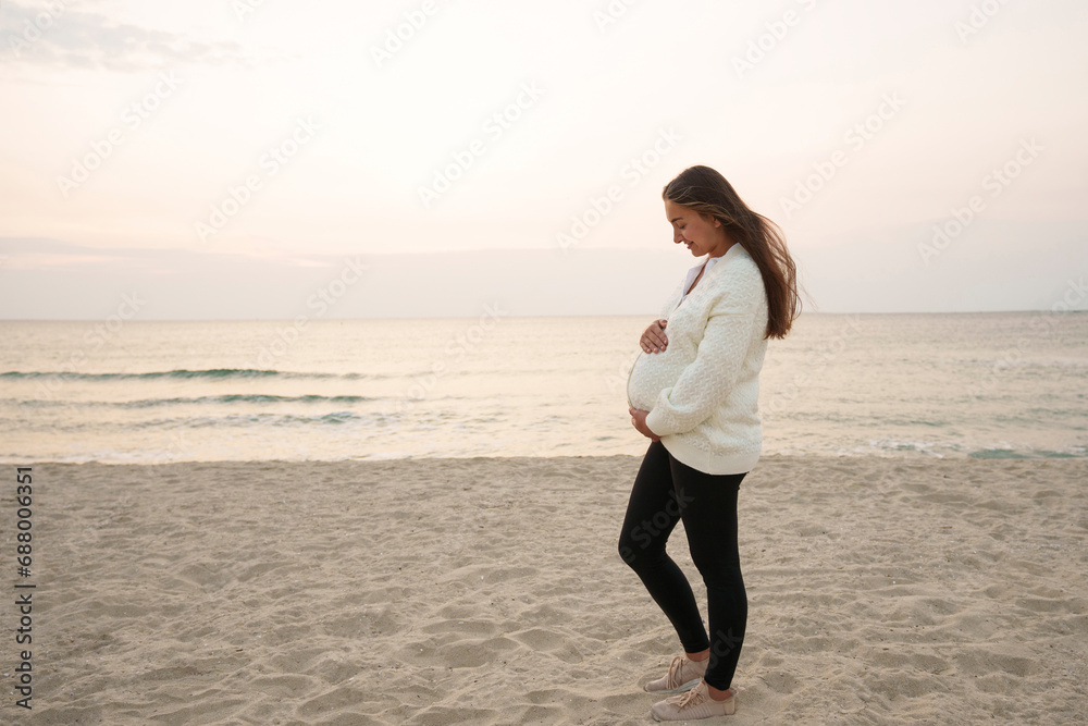 Happy pregnant woman standing with hands on abdomen at beach Happy pregnant woman standing with hands on abdomen at beach