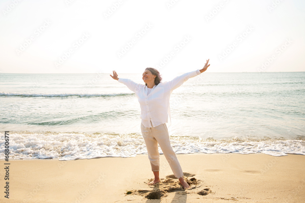 Carefree mature woman with arms outstretched standing at beach Carefree mature woman with arms outstretched standing at beach
