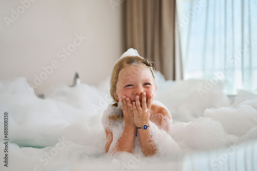 Blond girl covering mouth and laughing in bathtub photo