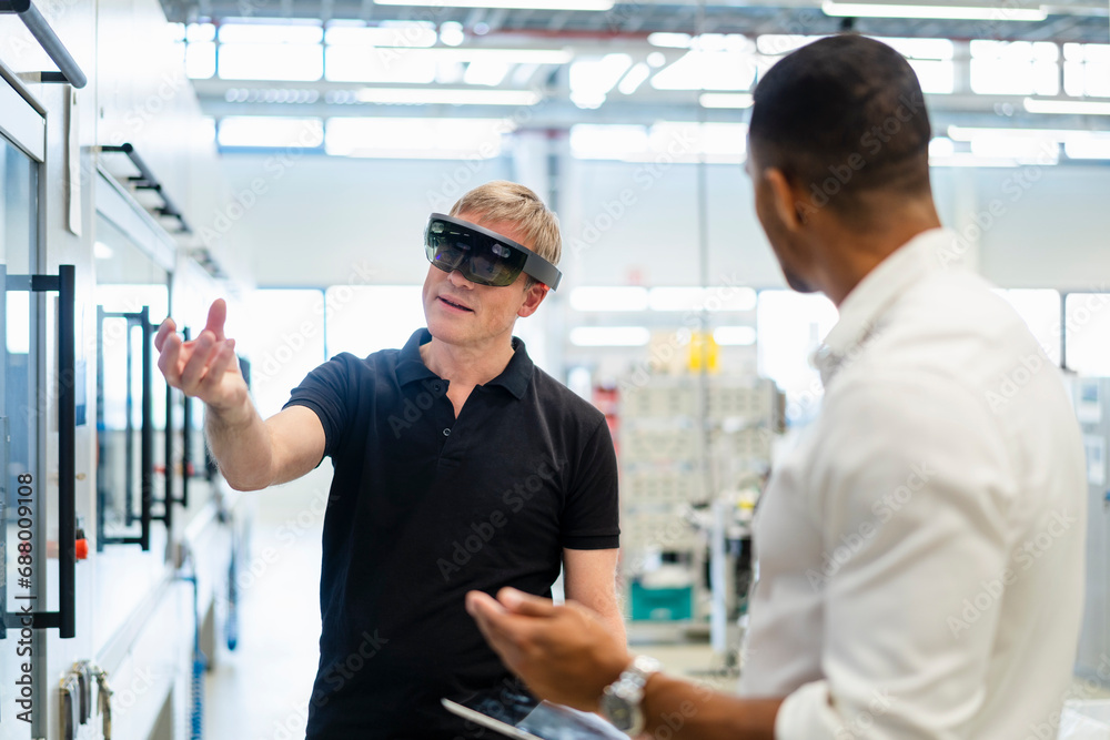 Technician wearing augmented reality glasses in a factory interacting with colleague Technician wearing augmented reality glasses in a factory interacting with colleague