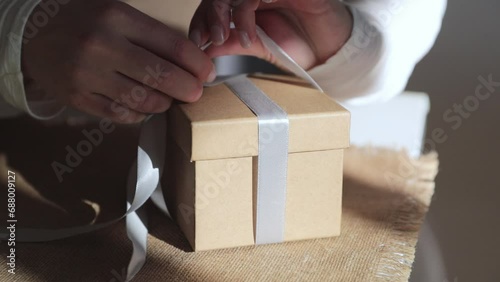 hands tying a box with a gift with a bow, holiday gift concept, preparation for birthday or Christmas celebration. close shot