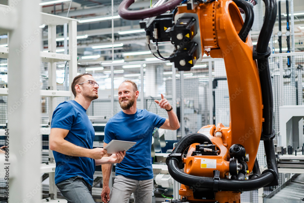 Two technicians with digital tablet examining industrial robot in a factory Two technicians with digital tablet examining industrial robot in a factory