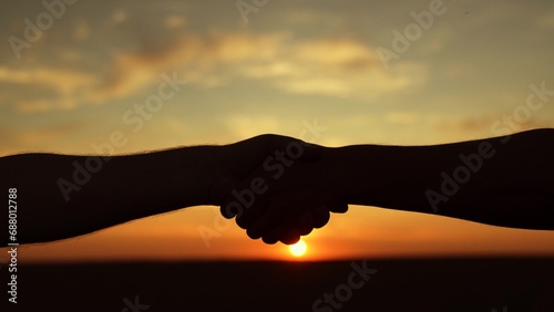 Handshake of two businessmen colleagues against background of sun, silhouette of two hands in nature. Business through handshake. Conclusion of deal. Handshake agreed. Business people shake hands, sky