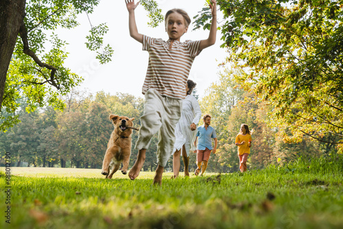 Playful boy running with dog and family on grass at park photo