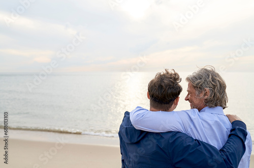 Happy father and son with arm around each other at beach photo