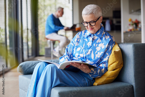 Senior woman sitting on couch at home reading magazine photo
