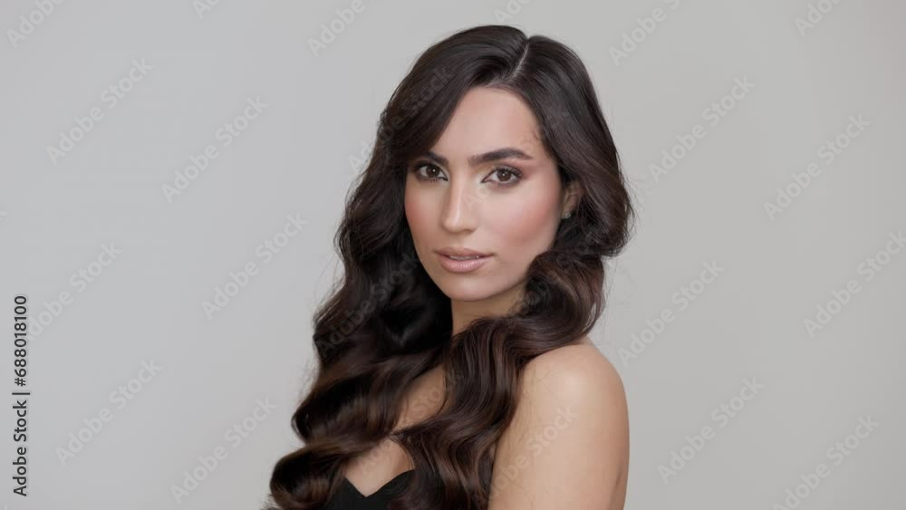 Young charming brunette with long wavy hair posing on a light gray background.