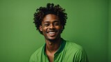 african american young man with curly hairstyle, smiling and laughing, wearing bright green clothes at bright solid green background
