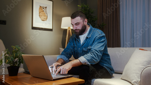 Young adult freelancer man working from home with using laptop while sitting on sofa at home