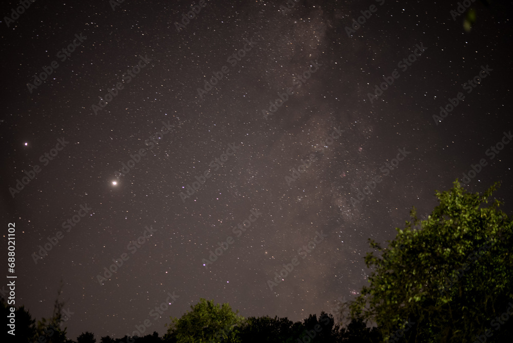 The milky way galaxy observed from a dark place in the middle of the wild forest. Planet Jupiter and Saturn in conjunction in a starry night sky