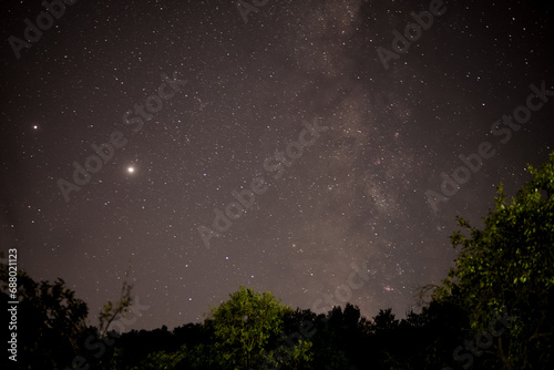 The milky way galaxy observed from a dark place in the middle of the wild forest. Planet Jupiter and Saturn in conjunction in a starry night sky