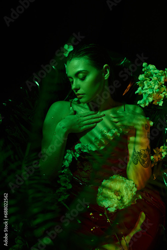 green light, charming young woman with wet hair looking away and posing among flowers, elegance