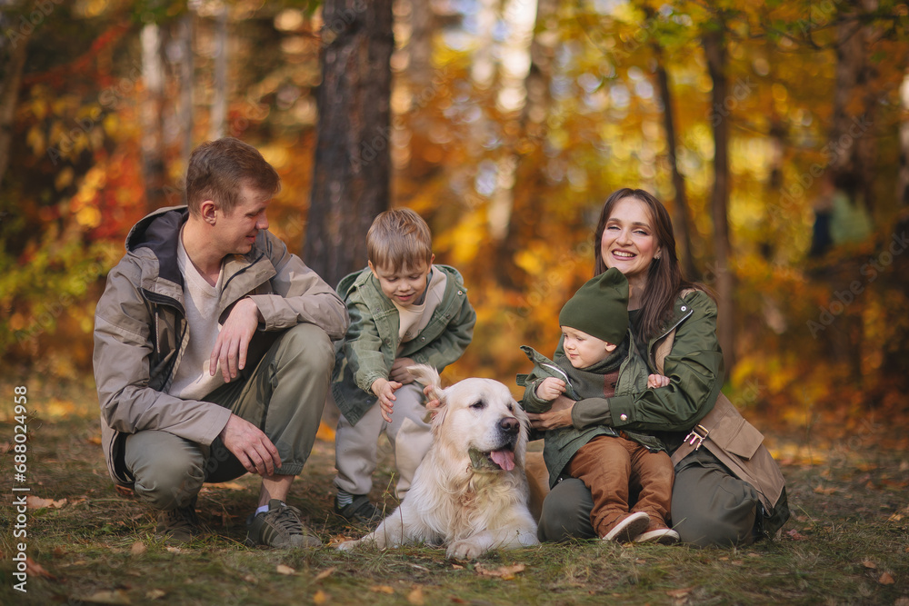 Smiling beautiful family of four walking in the park with a happy golden retriever and enjoying the beautiful autumn nature. Smiling beautiful family of four walking in the park with a happy golden retriever and enjoying the beautiful autumn nature.