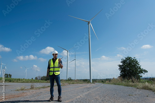 engineer with turbine in background. Service engineers checking wind turbine on tablet on  wind turbine farm Power Generator  on background Station on mountain  Thailand people