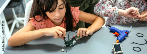 Concentrated female student screwing electrical circuit next to schoolchild in a robotics class. Elementary technological education concept. photo