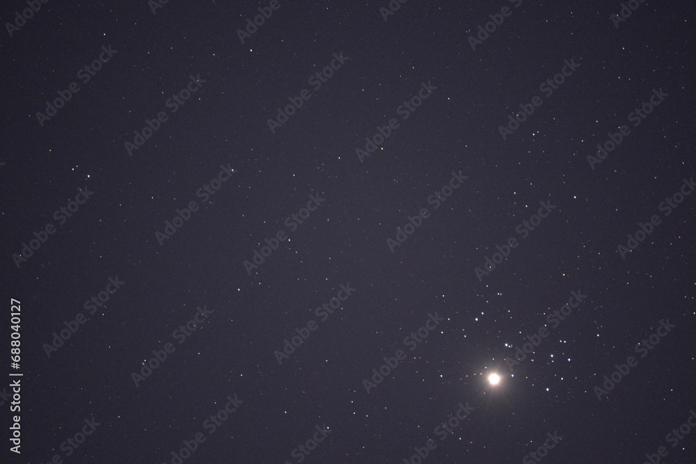 The planet Venus in the starry night sky in conjunction with the Pleiades Constellation. The group of stars The seven sisters observed from a dark place