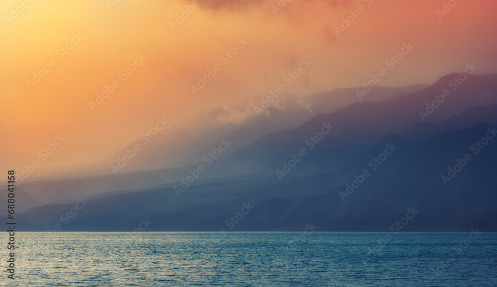 sea or lake in foggy haze at the foot of beautiful mountains at sunset