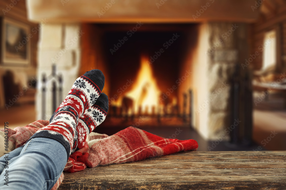 Woman legs with warm winter socks. Home interior with fireplace and empty space for your decoration. Mockup background and december time. Cold winter and new year. Woman legs with warm winter socks. Home interior with fireplace and empty space for your decoration. Mockup background and december time. Cold winter and new year.