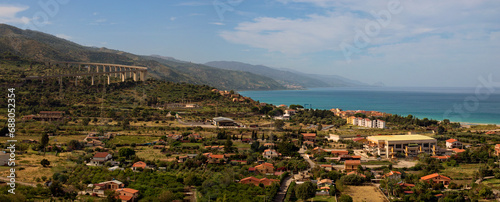 Picturesque panoramic landscape view of Sicily at sunny day. Curved automobile viaduct in mountains near Santo Stefano di Camastra. Small houses near the sea. Travel and tourism concept. Sicily, Italy