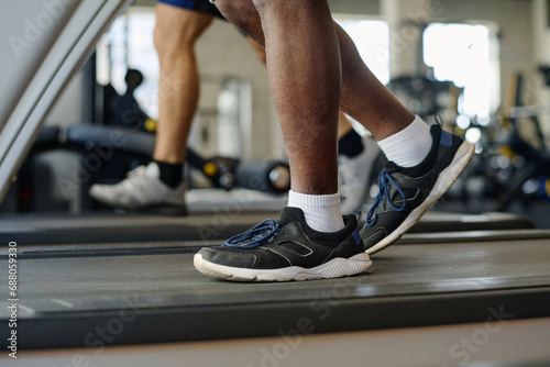 Feet of unknown man in sneakers walking on treadmill with another person training on background © AnnaStills