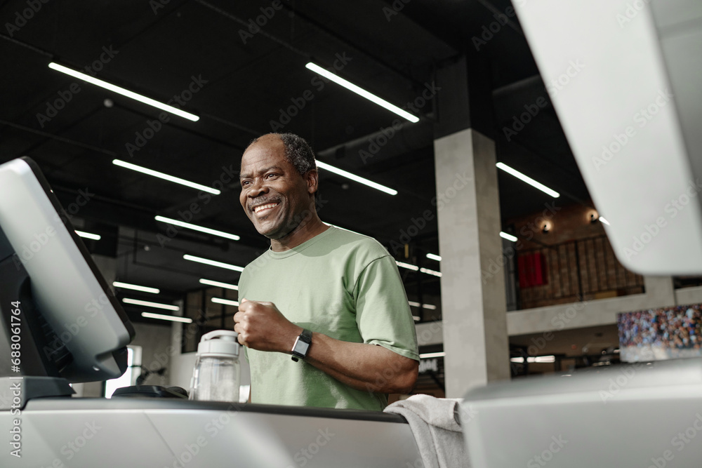 Medium low angle shot of happy senior african american runner training on treadmill at gym Medium low angle shot of happy senior african american runner training on treadmill at gym