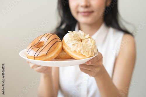 Close up donut plate with happy smile asian young woman, girl temptation food, enjoy eating sugar glazed doughnut and delicious dessert sweet, snack tasty. Eat fast food, junk food meal getting fat.