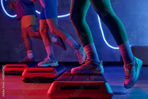 Unknown gym goer stepping onto step platform with one leg with sportspeople exercising on background