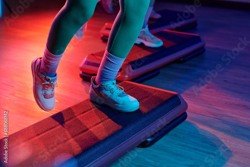 Unknown sportsperson exercising on step platform at gym with other people training on background