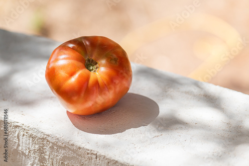 A big tomato of variety Belmonte silano on the concrete wall on the blurred natural background, copy space. It is the typical Calabrian tomato grown on Mount Sila, Calabria photo