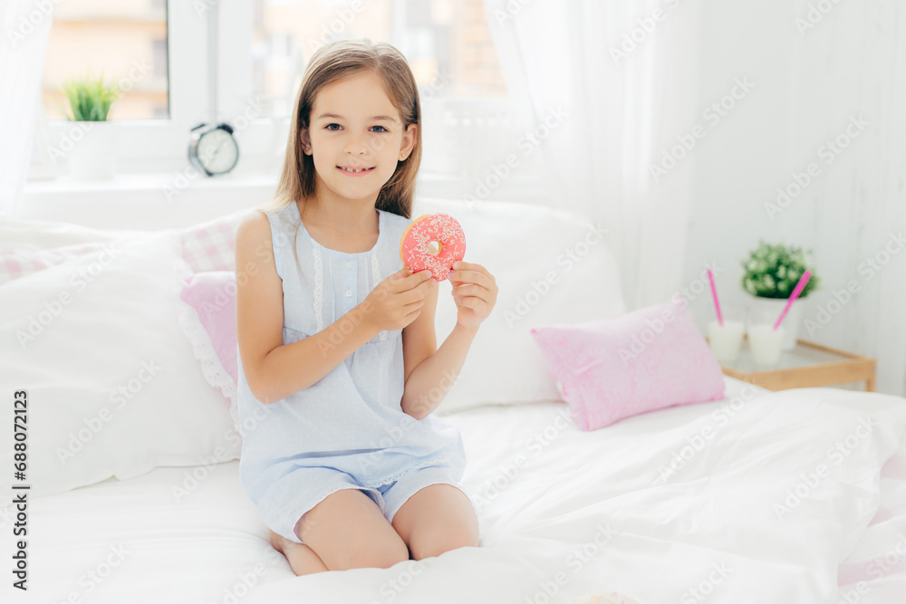 Happy young girl holding a donut in a bright and cozy bedroom