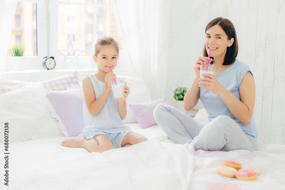 Mother and daughter enjoying milkshakes in a bright bedroom setting