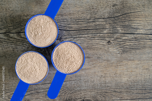 Supplement scoops in formation filled with protein powder on top of wooden kitchen surface. Dietary and athletic nutrition concept – flat lay, top view with copy space.