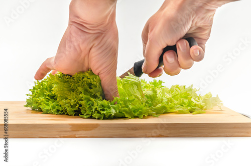 Cutting fresh green salad on a wooden kitchen board. Side view. Female hands with a knife.