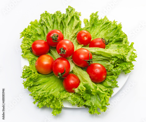 Green fresh lettuce leaves with juicy cherry tomatoes in a white bowl. Isolated on white background.