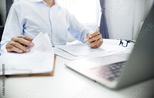 Businessman or lawyer holding pencil reviewing business documents or contract. working online with laptop and contact customer to give advice about business contracts, insurance