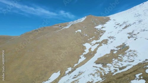 Aerial view of high mountains covered with snow with thawing on a sunny day against a sky. Deserted gray mountains in winter without grass with snowy peaks. Drone footage. Movement in an arc. Armenia