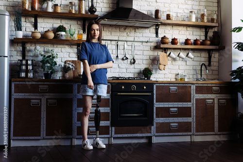 Lady with prosthetic limb stands in kitchen with crossed arms photo