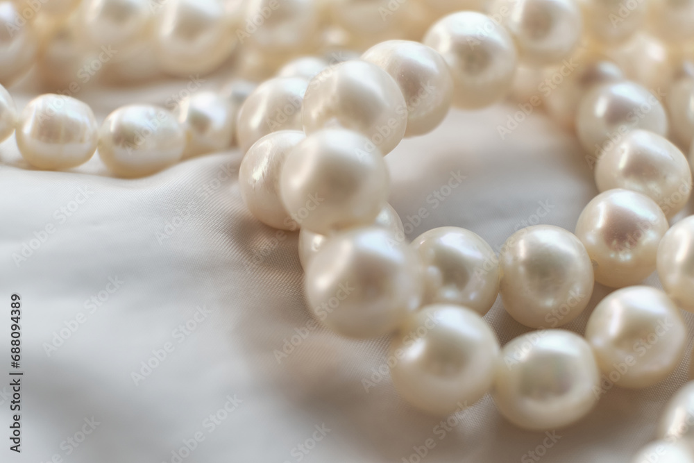 A string of pearls gracefully rests on a white backdrop, blurring softly at the edges. The image is a quaint juxtaposition to the sharp, high-definition visuals trending in today's digital landscape.