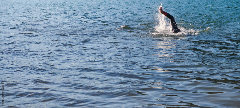 Fototapeta premium Triathlon athlete swimming on lake in sunrise wearing wetsuit