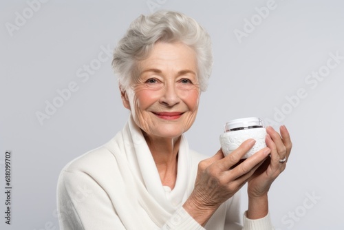 A smiling elderly woman holds a cream jar, radiating joy and emphasizing the importance of skincare in the aging process