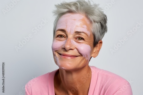 Against a backdrop of purity, a woman with cream on her face emphasizes the care and self-love involved in the aging skincare routine photo