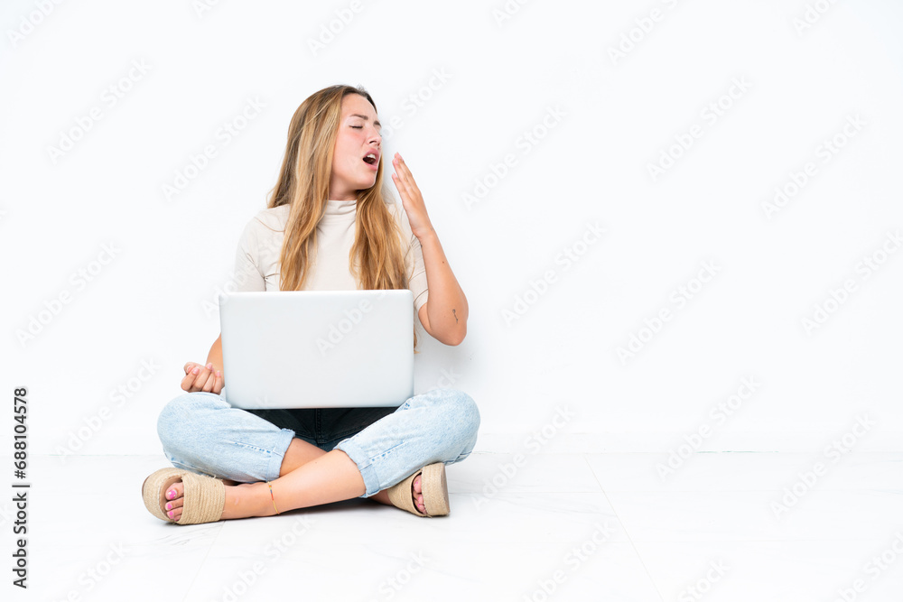 Young woman with laptop sitting on the floor isolated on white background yawning and covering wide open mouth with hand Young woman with laptop sitting on the floor isolated on white background yawning and covering wide open mouth with hand