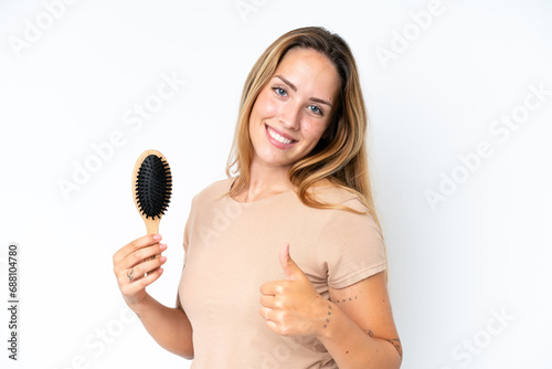 Young caucasian woman with hair comb isolated on white background with thumbs up because something good has happened