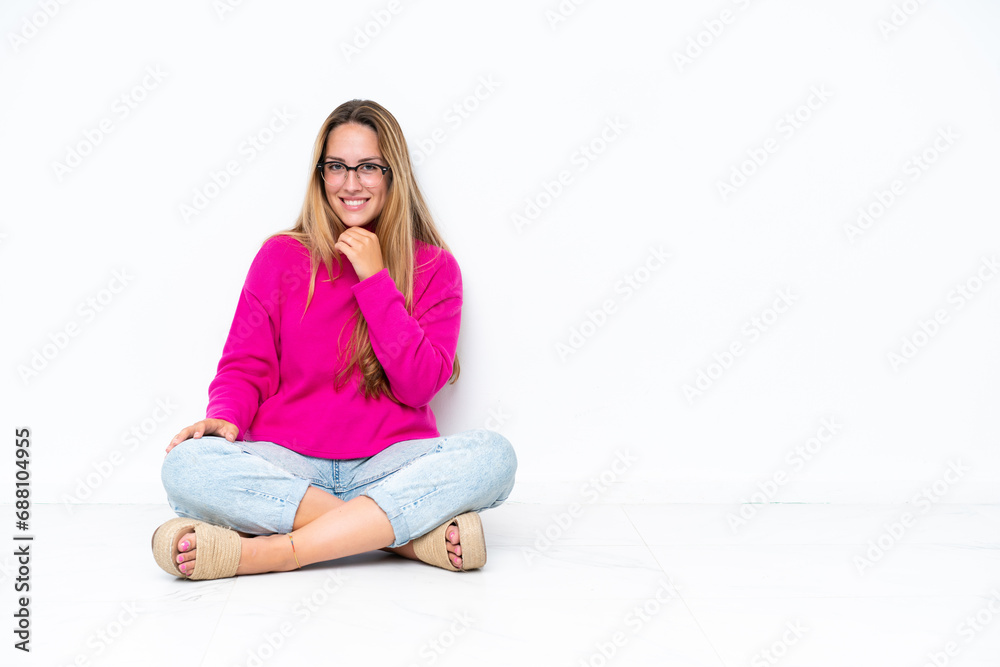 Young caucasian woman sitting on the floor isolated on white background with glasses and smiling